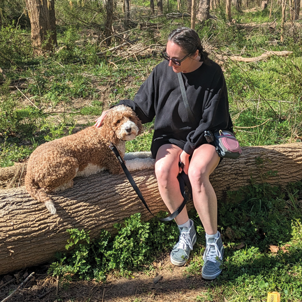  A woman and her brown dog sit upon a log in a park setting.